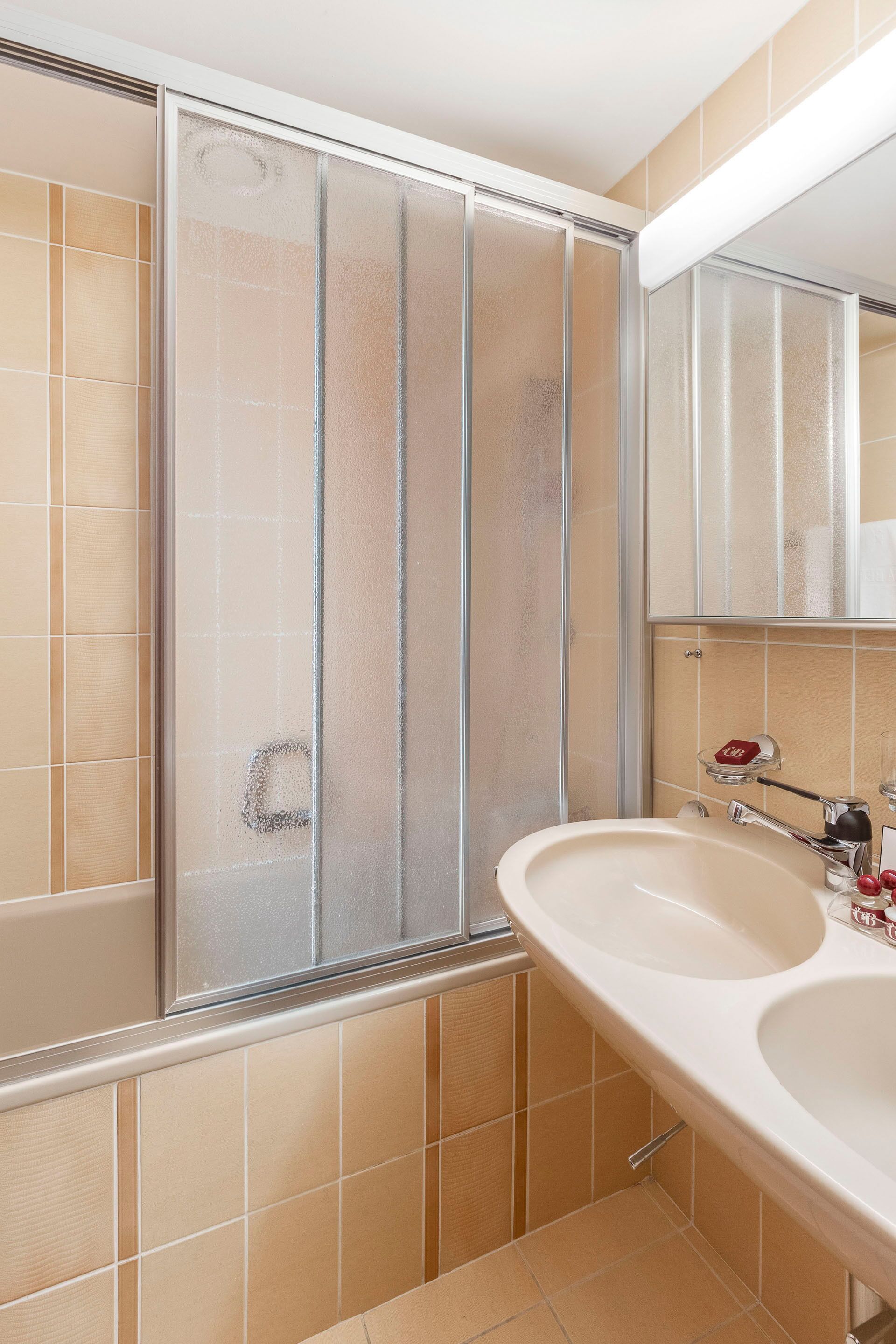 A bathroom with a glass shower enclosure, a sink, and a mirror.