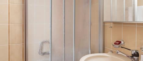A bathroom with a glass shower enclosure, a sink, and a mirror.