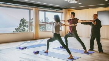 A spacious room with large windows, wooden floors, and yoga mats arranged for a group exercise class.