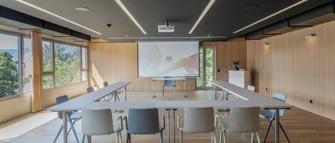 A conference room with a long table, chairs, a projector screen, and large windows.