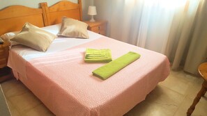 A neatly made bed with a pink patterned bedspread, two pillows, and a green towel. - Hostal El Peine (Torrejón de Ardoz)