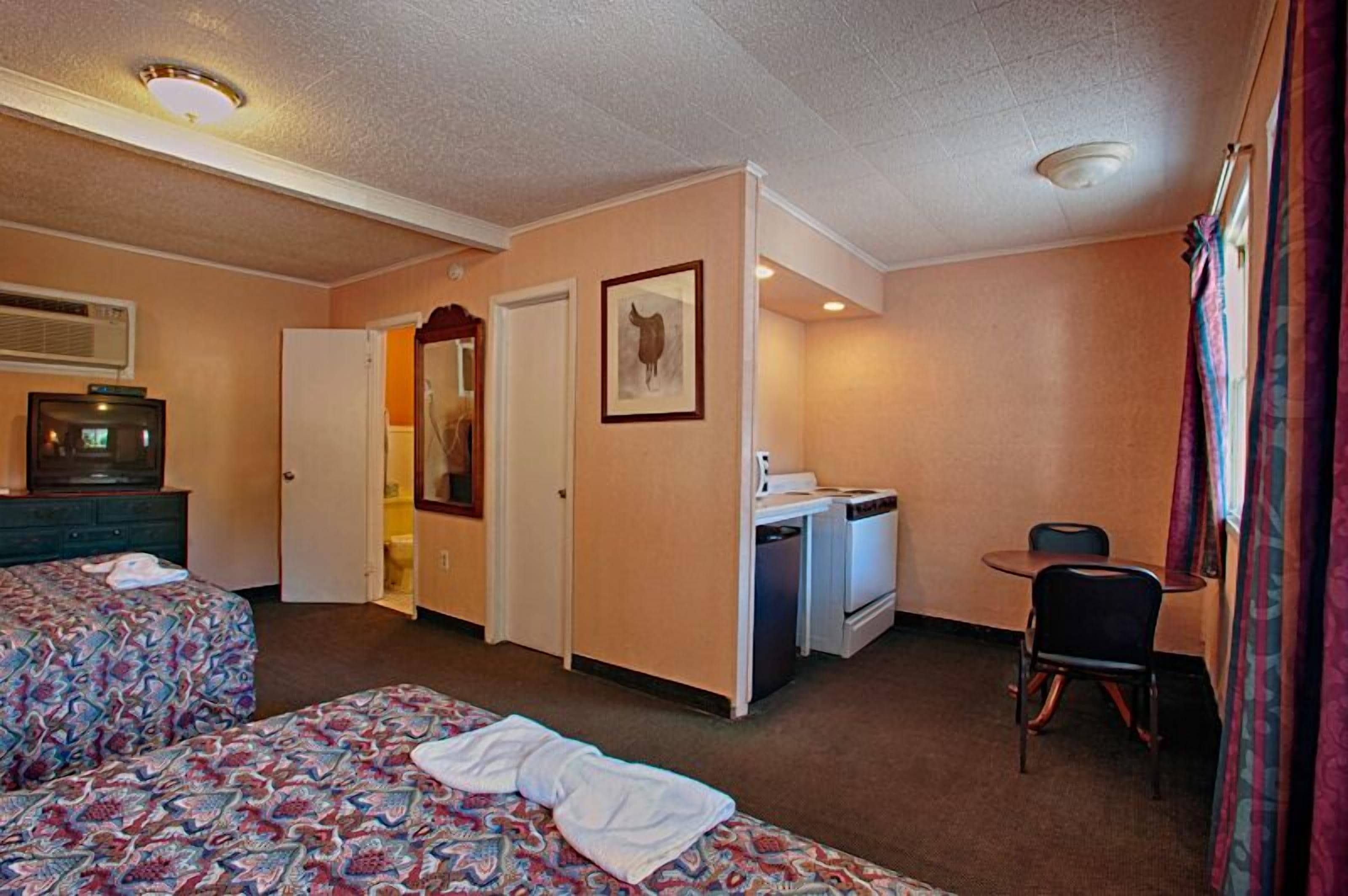 A hotel room with two beds, a desk with a chair, a microwave, and a small kitchenette.