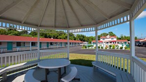 A covered outdoor area with a table and benches, overlooking a motel with multiple rooms and a parking lot. - Economy Motel Inn & Suites (Somers Point)