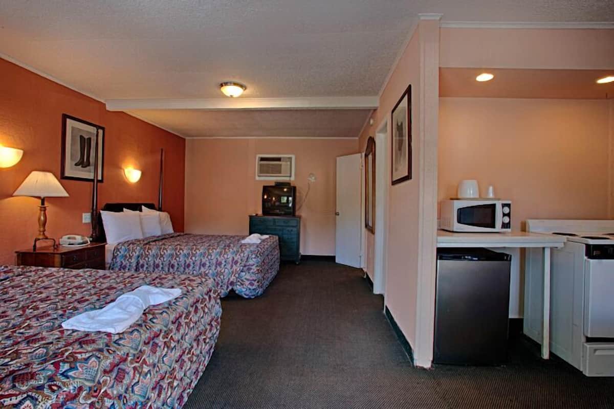 A hotel room with two beds, a desk with a microwave, a refrigerator, and a small kitchenette.