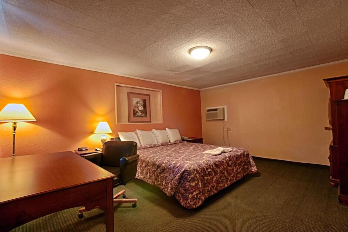 A hotel room with a bed, two bedside lamps, a desk, a chair, and a dresser.
