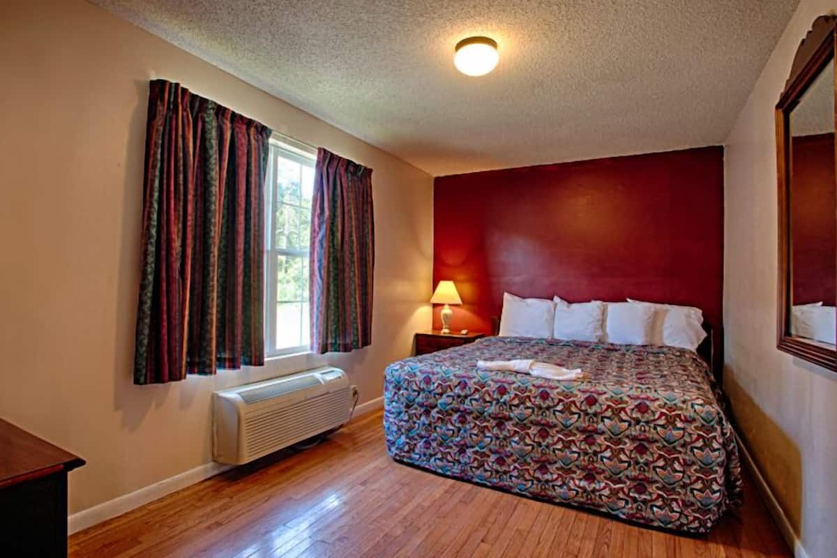 A bedroom with a bed, a window with curtains, a bedside lamp, and a radiator.
