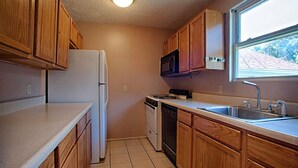 A compact kitchen with wooden cabinets, a refrigerator, stove, microwave, and a sink. - Economy Motel Inn & Suites (Somers Point)
