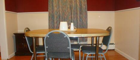 A dining area with a round wooden table, four chairs, a white trash bin, and a curtain with a wavy pattern.
