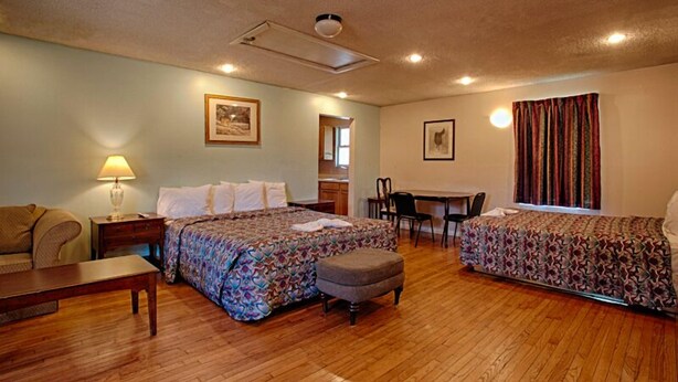 A room with two beds, a desk, a chair, a lamp, and a window with curtains. - Economy Motel Inn & Suites (Somers Point)