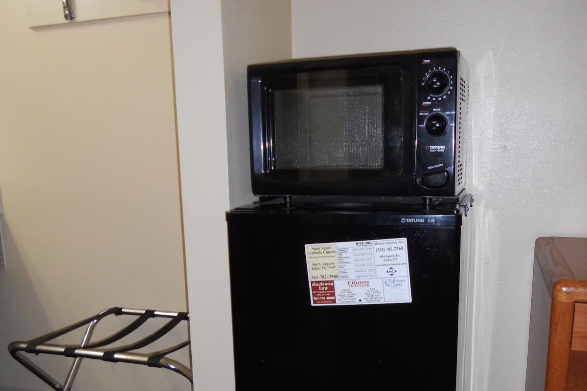 A compact black refrigerator with a microwave on top, a metal drying rack, and a wooden chair.