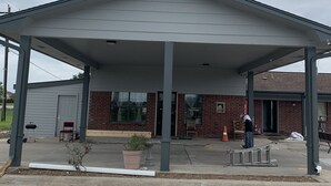 Un bâtiment doté d’une entrée abritée, d’une façade en briques et d’un petit jardin agrémenté d’un banc et de plantes en pot.