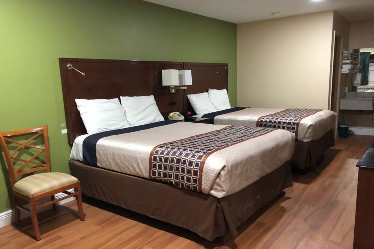 A hotel room with two beds, wooden headboards, a chair, and a small desk.