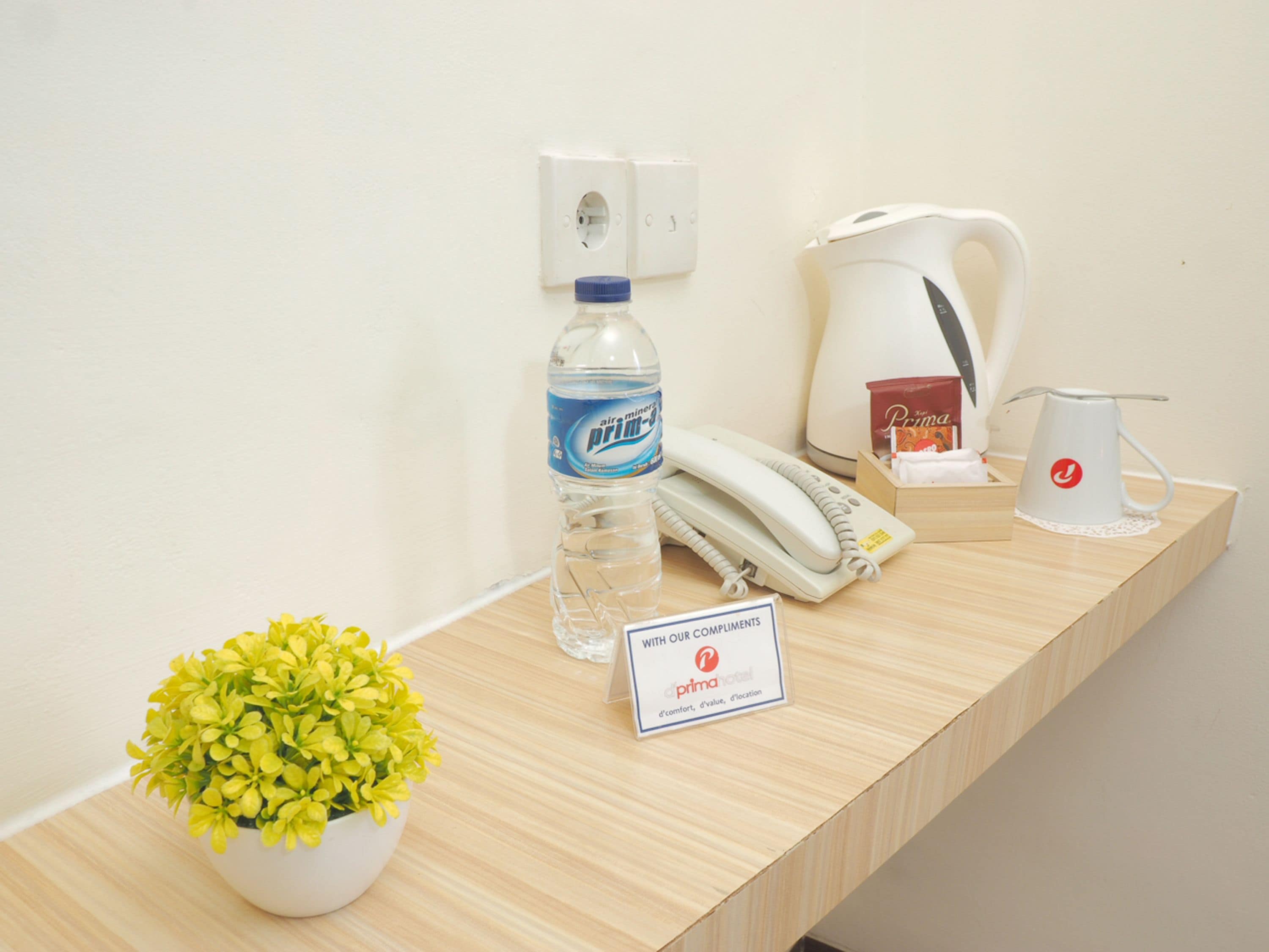 Un mostrador de recepción con una botella de agua, un teléfono, una cafetera, un cartel y una planta en maceta.