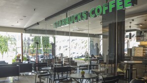 Ein Starbucks Kaffeehaus mit modernem Interieur, Glastrennwänden und verschiedenen Sitzgelegenheiten, darunter Tische und Stühle.