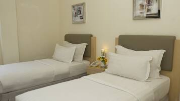 A hotel room with two single beds, a bedside table with a lamp, and two framed pictures on the wall.