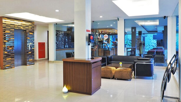 A modern lobby with a reception desk, seating area, and a visible coffee shop in the background. - d'primahotel ITC Mangga Dua (Jakarta)
