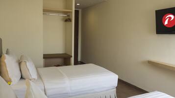 A hotel room with two beds, a wardrobe, a TV on the wall, and a shelf.