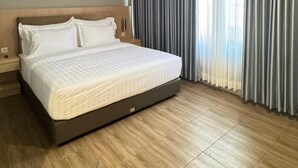 A modern hotel room with a large bed, wooden flooring, and a view of the city through sheer curtains. - d'primahotel ITC Mangga Dua (Jakarta)