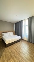 Quarto de hotel moderno com uma cama grande, piso de madeira e vista da cidade através de cortinas leves.