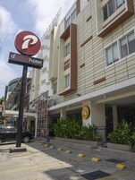 Um hotel com design moderno, exibindo uma placa grande com 'd'primahotel', um logotipo com um chef e uma área externa bem cuidada com plantas e um estacionamento.