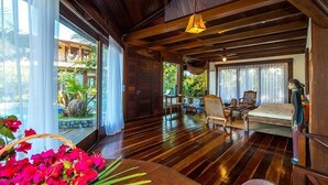 A spacious room with wooden floors, a large window with curtains, a bed, and a seating area with chairs and a table. - Sombra e Água Fresca Resort (Tibau do Sul)