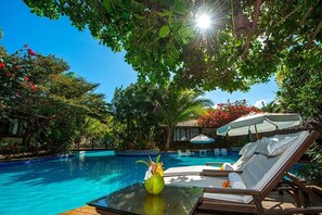 A poolside area with lounge chairs, a table with a vase, and a pool surrounded by lush greenery. - Sombra e Água Fresca Resort (Tibau do Sul)