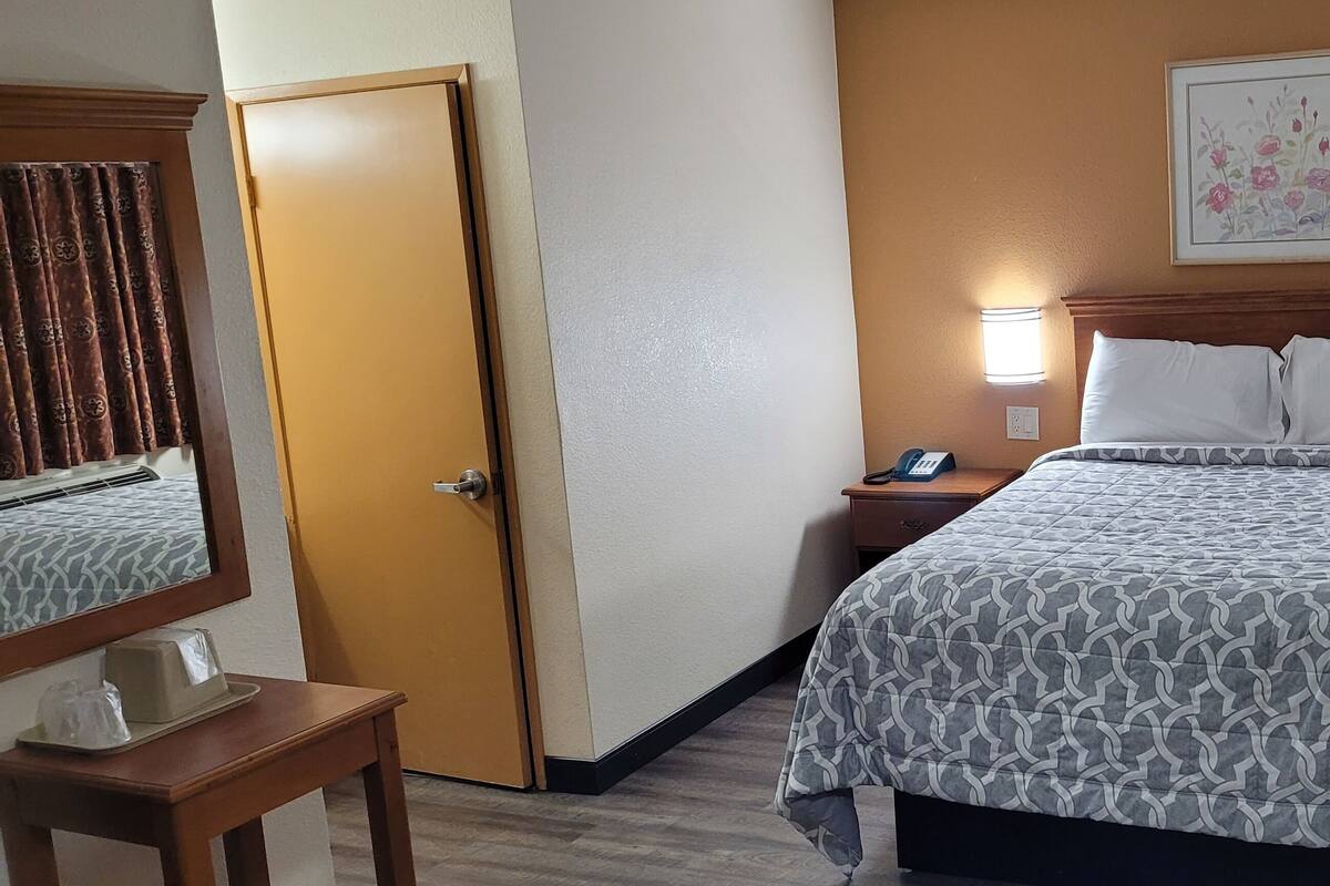 A hotel room with a bed, bedside lamps, a nightstand, a telephone, and an air conditioning unit.
