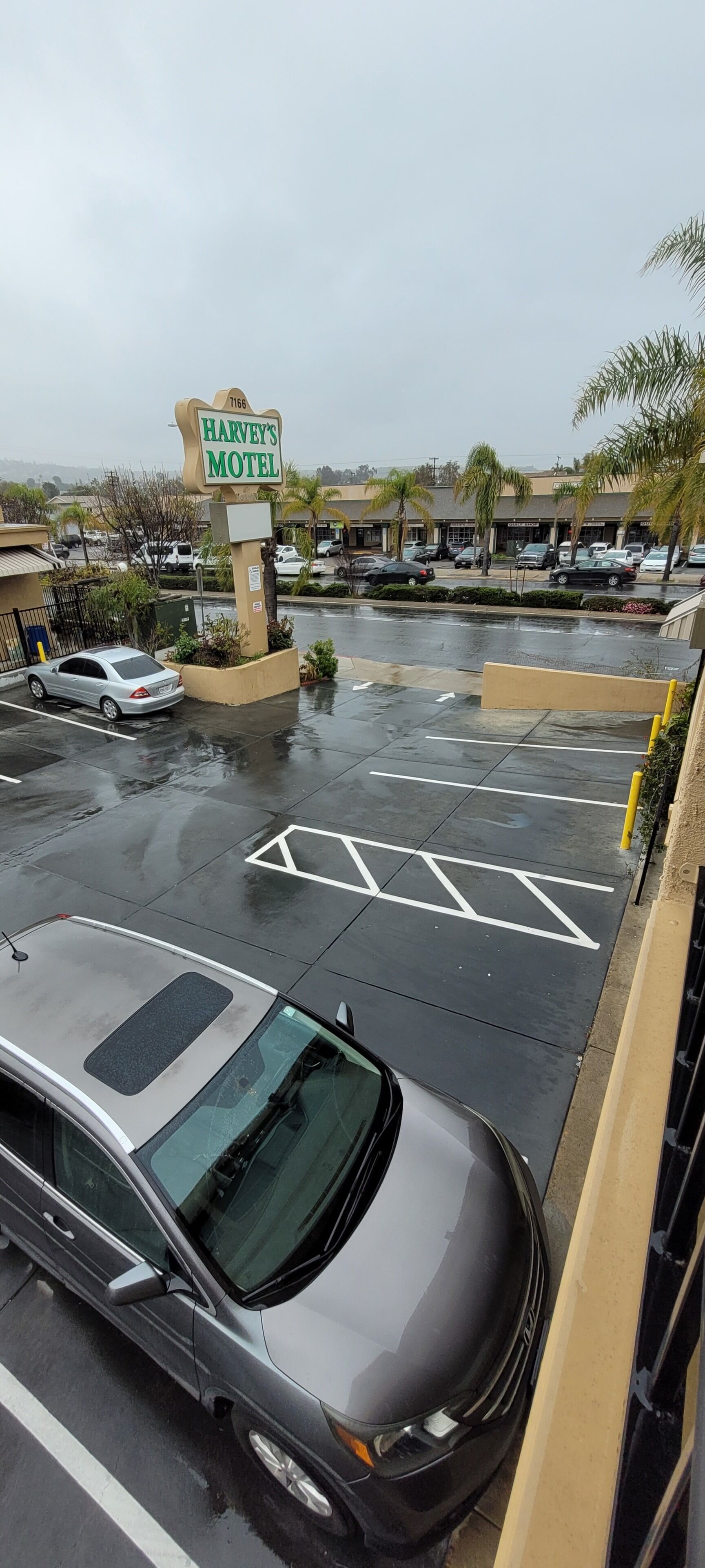 A parking lot with a sign for Harvey's Motel, multiple parked cars, and a wet pavement indicating recent rain.