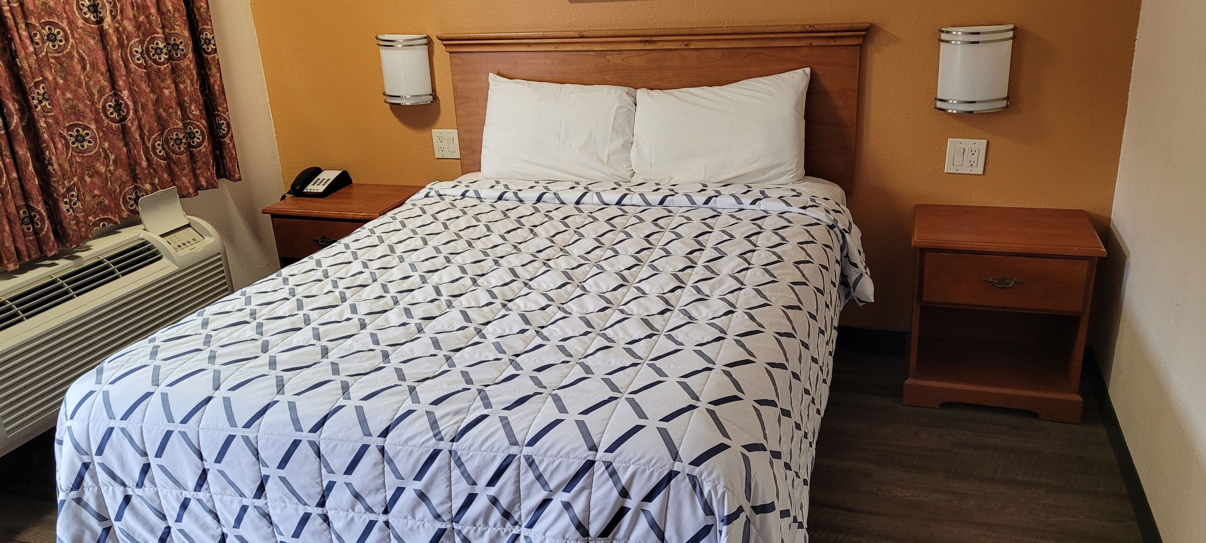 Una habitación de hotel con cama, mesita de noche con teléfono, calefactor y lámpara de pared.