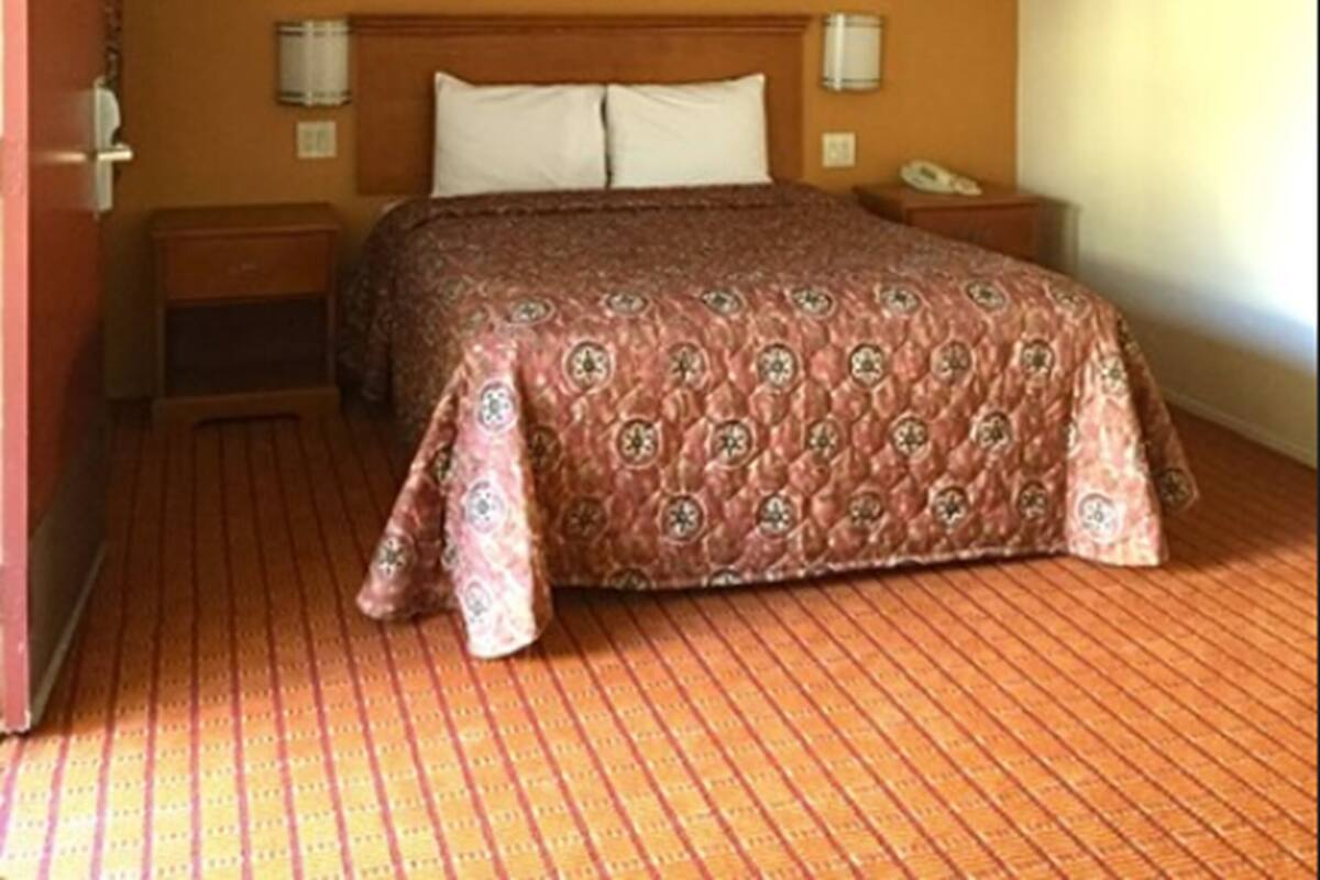 A hotel room with a bed, a nightstand, a wall-mounted lamp, and a framed picture on the wall.