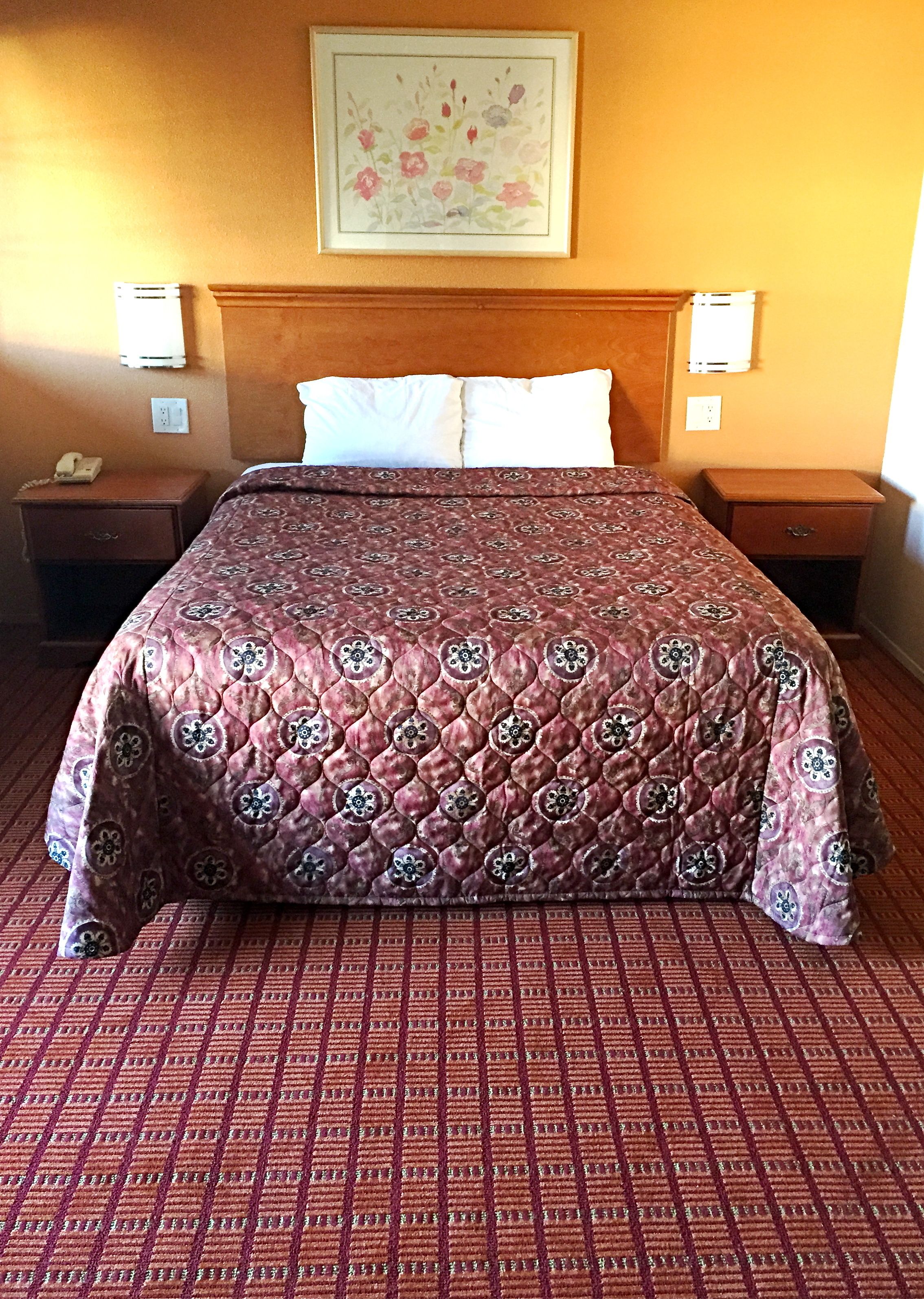 Una habitación de hotel con una cama grande, dos mesitas de noche, un teléfono y un cuadro en la pared.