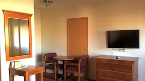 Une chambre d’hôtel avec une commode en bois, un téléviseur fixé au mur, une table ronde avec deux chaises et un miroir au-dessus de la commode.