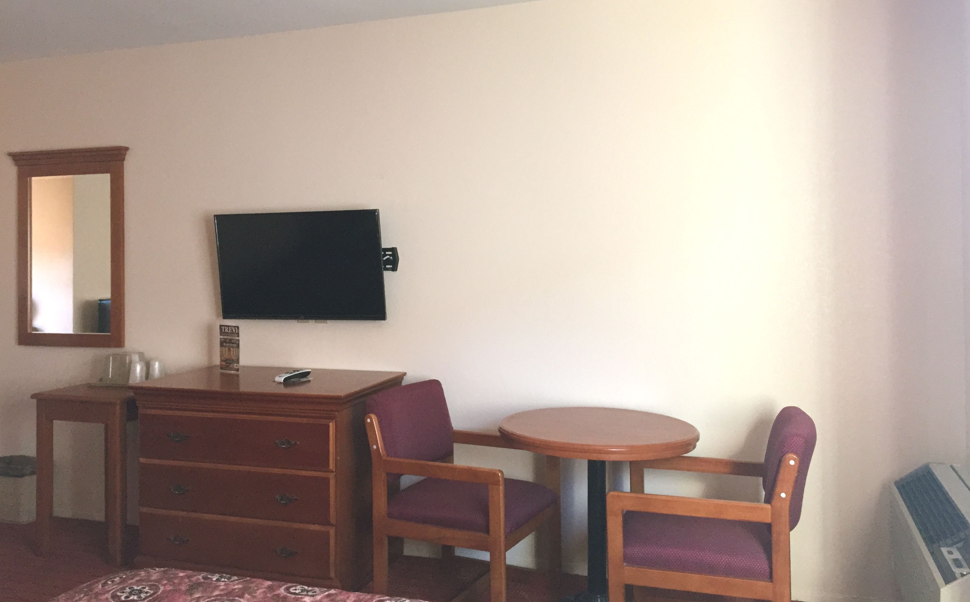 A hotel room with a wooden desk, two chairs, a television, and a mirror.
