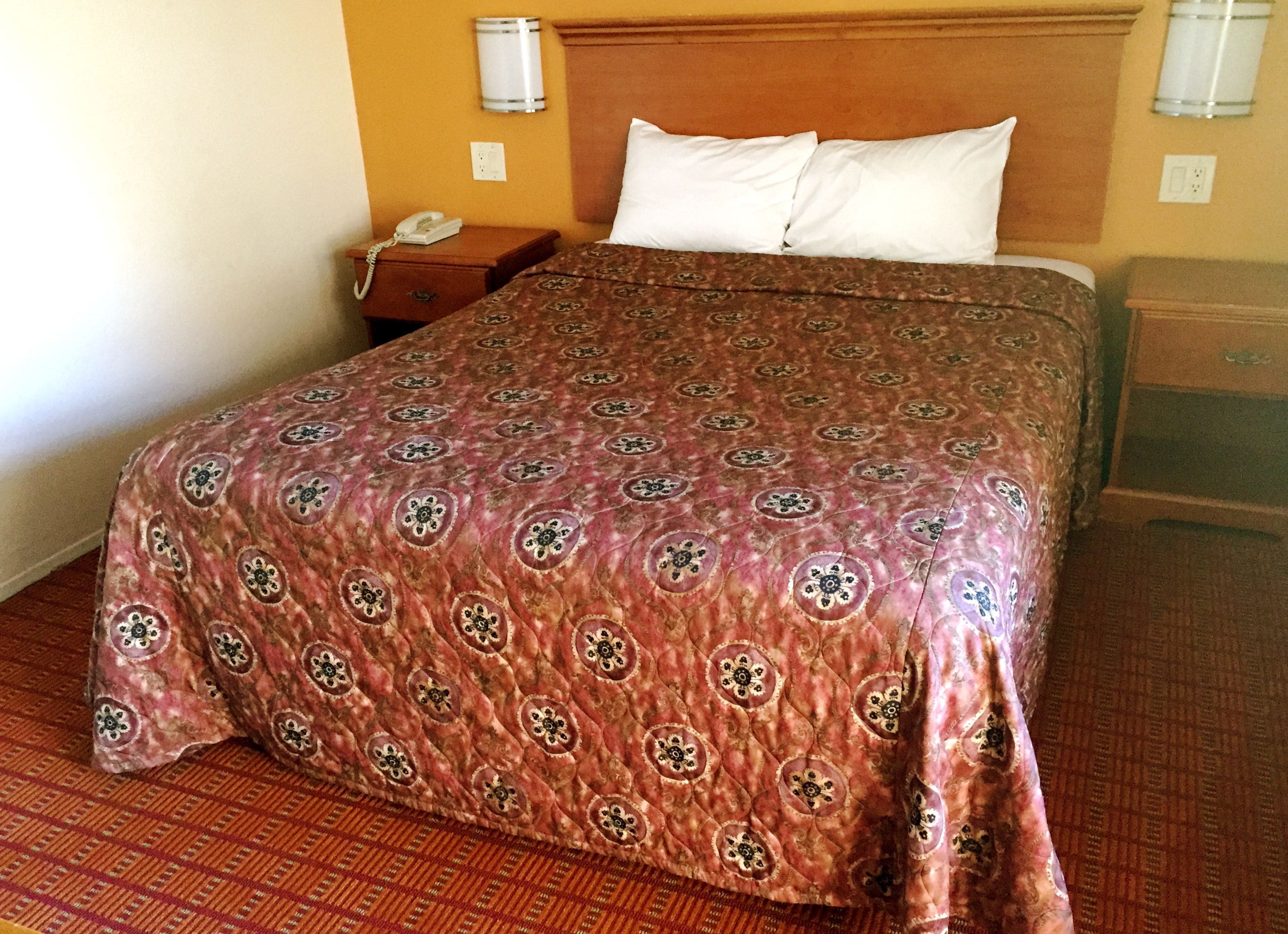 Ein Hotelzimmer mit einem Bett, einem Nachttisch, einem Telefon und einer wandmontierten Leuchte.