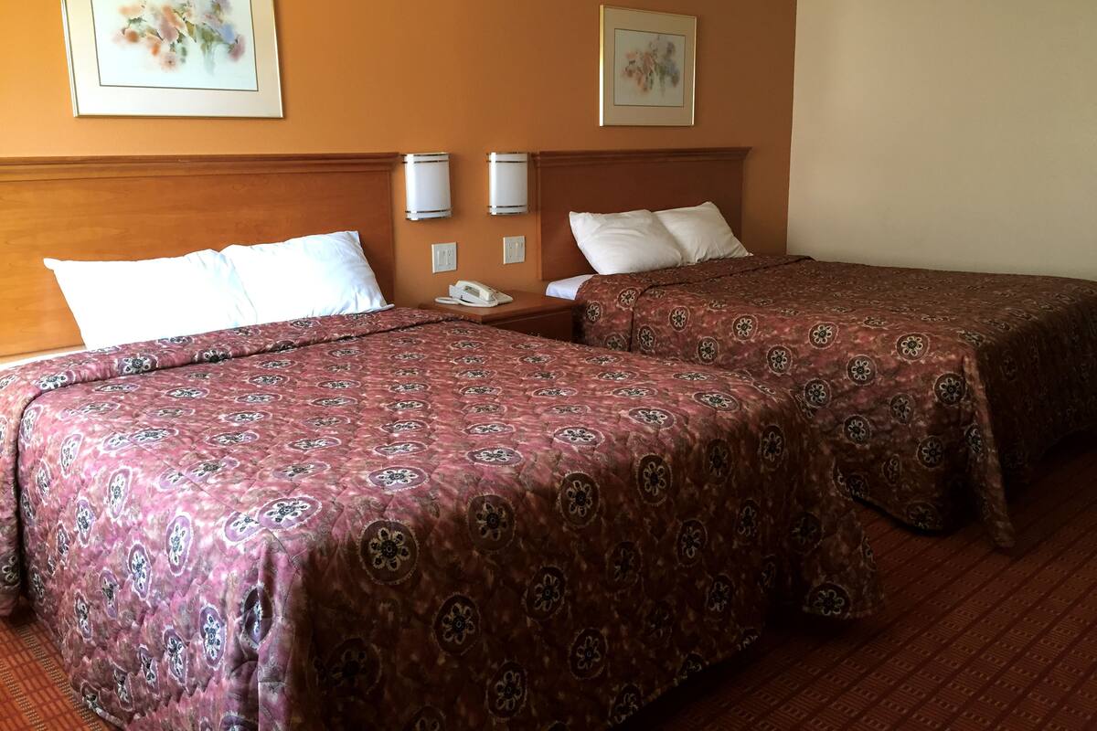 A hotel room with two beds, each with a patterned bedspread, a wooden headboard, a bedside table with a phone, and two wall-mounted light fixtures.
