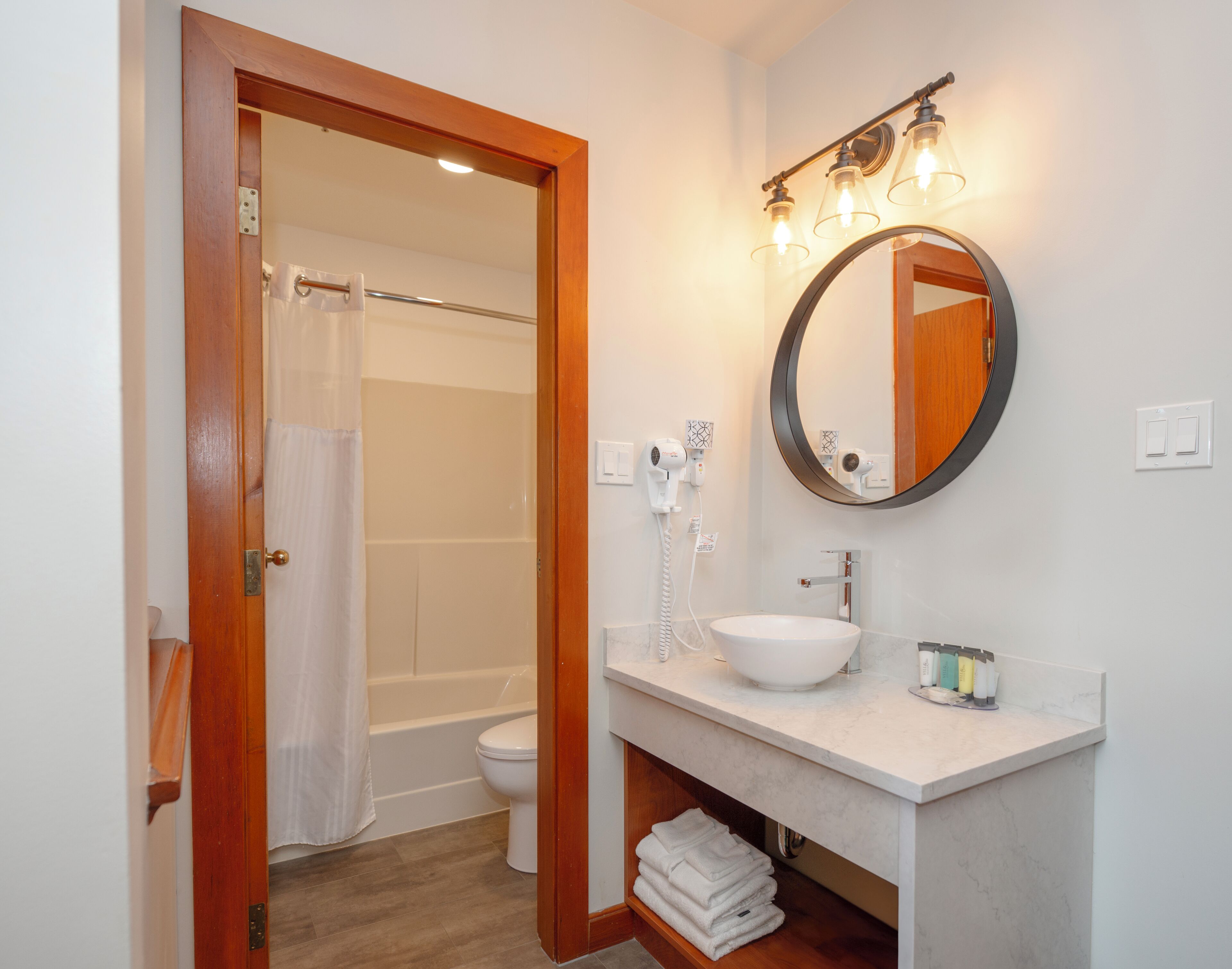 Un bagno con un lavandino bianco, uno specchio rotondo e un portasciugamani.