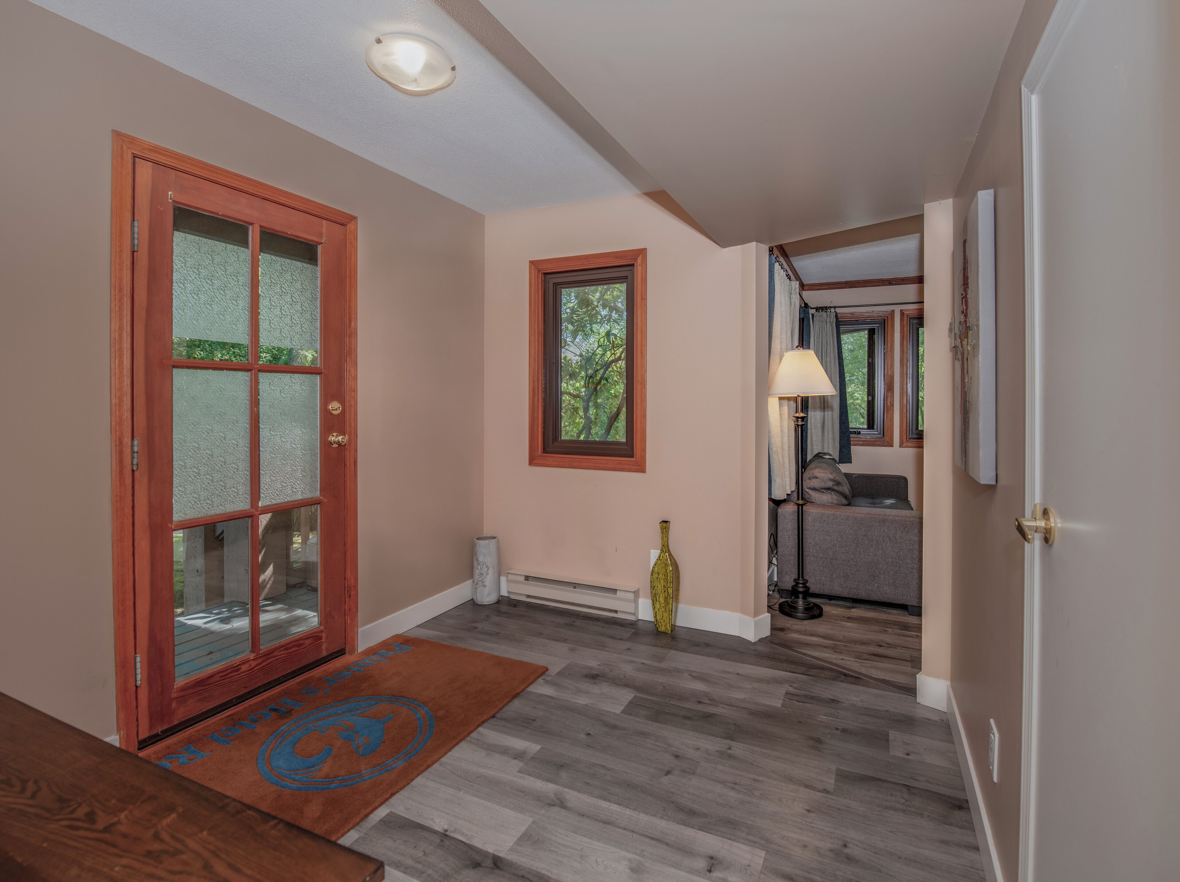A hallway with wooden flooring, a glass door, a window, and a lamp.