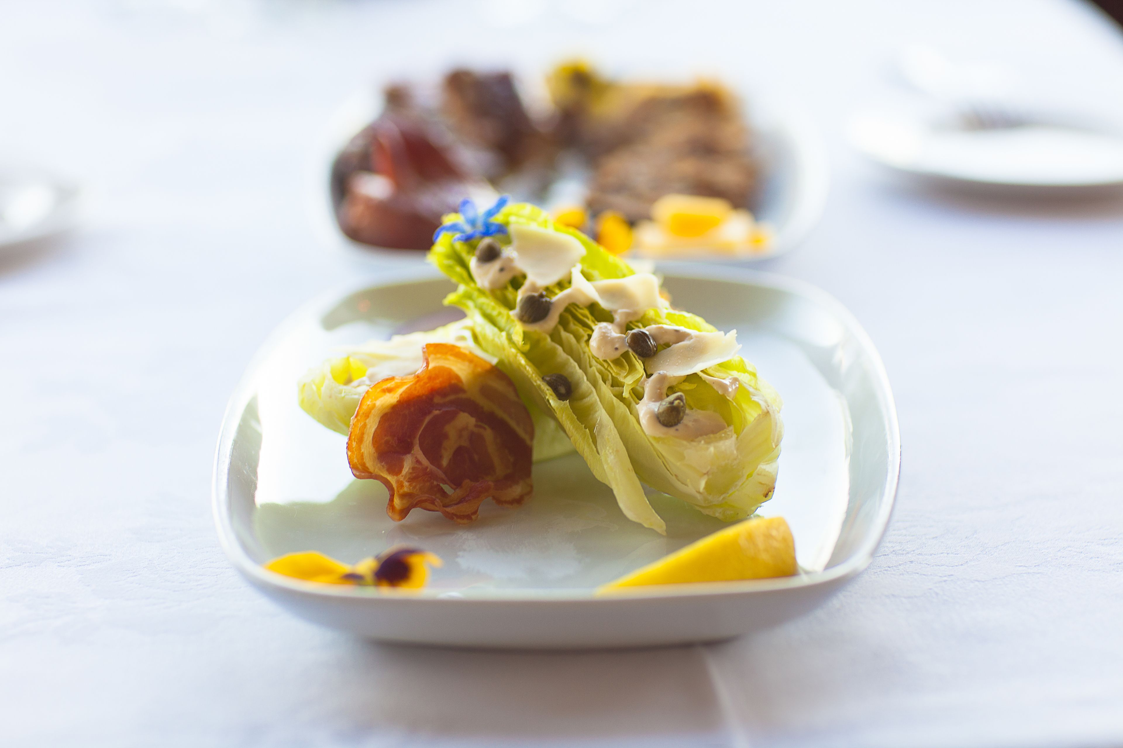Un plato con ensalada, una rodaja de naranja y un trozo de carne.
