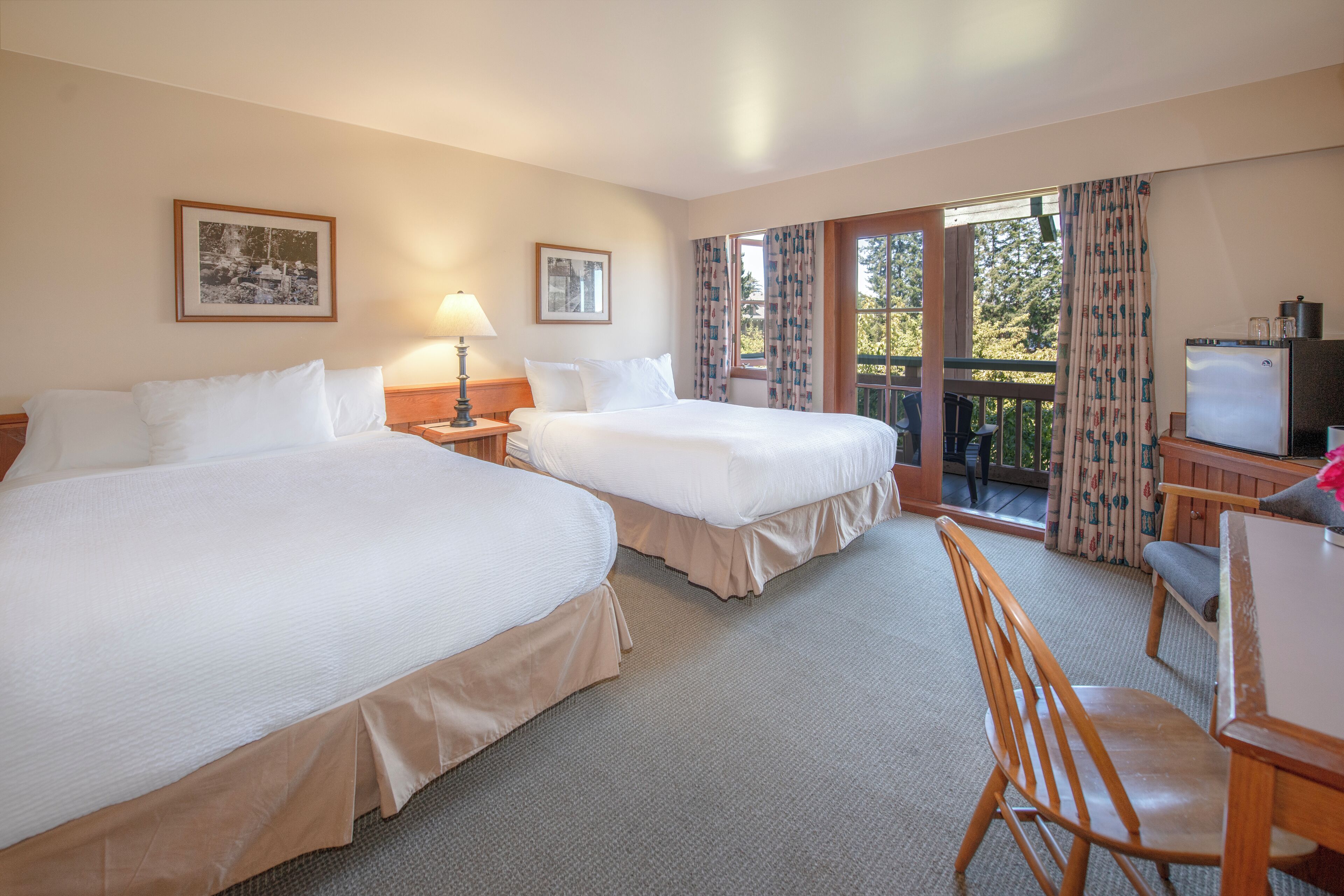 A hotel room with two beds, a desk, a chair, a television, and a balcony with curtains.