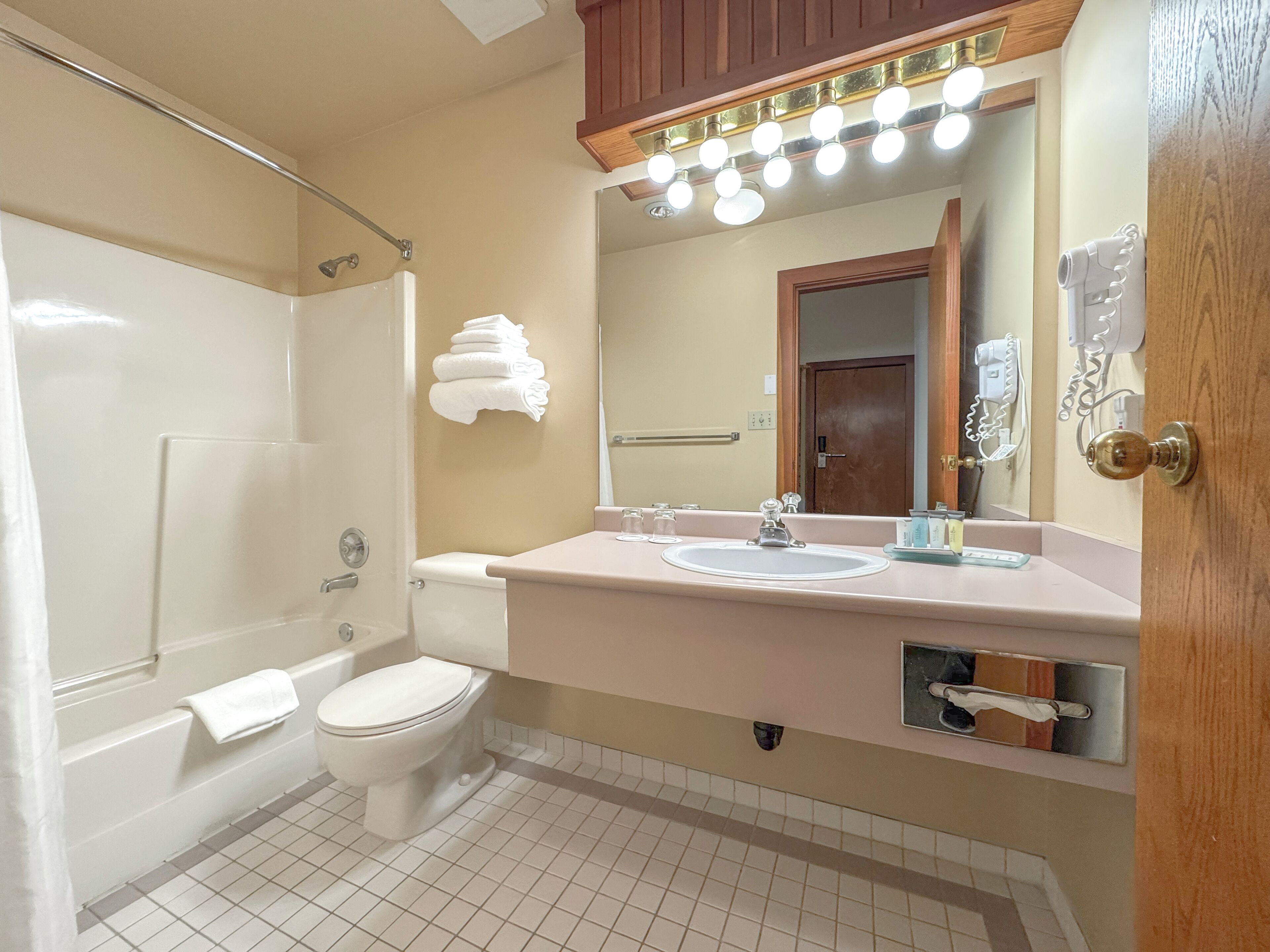 A bathroom with a bathtub, toilet, sink, and a mirror with lights above.