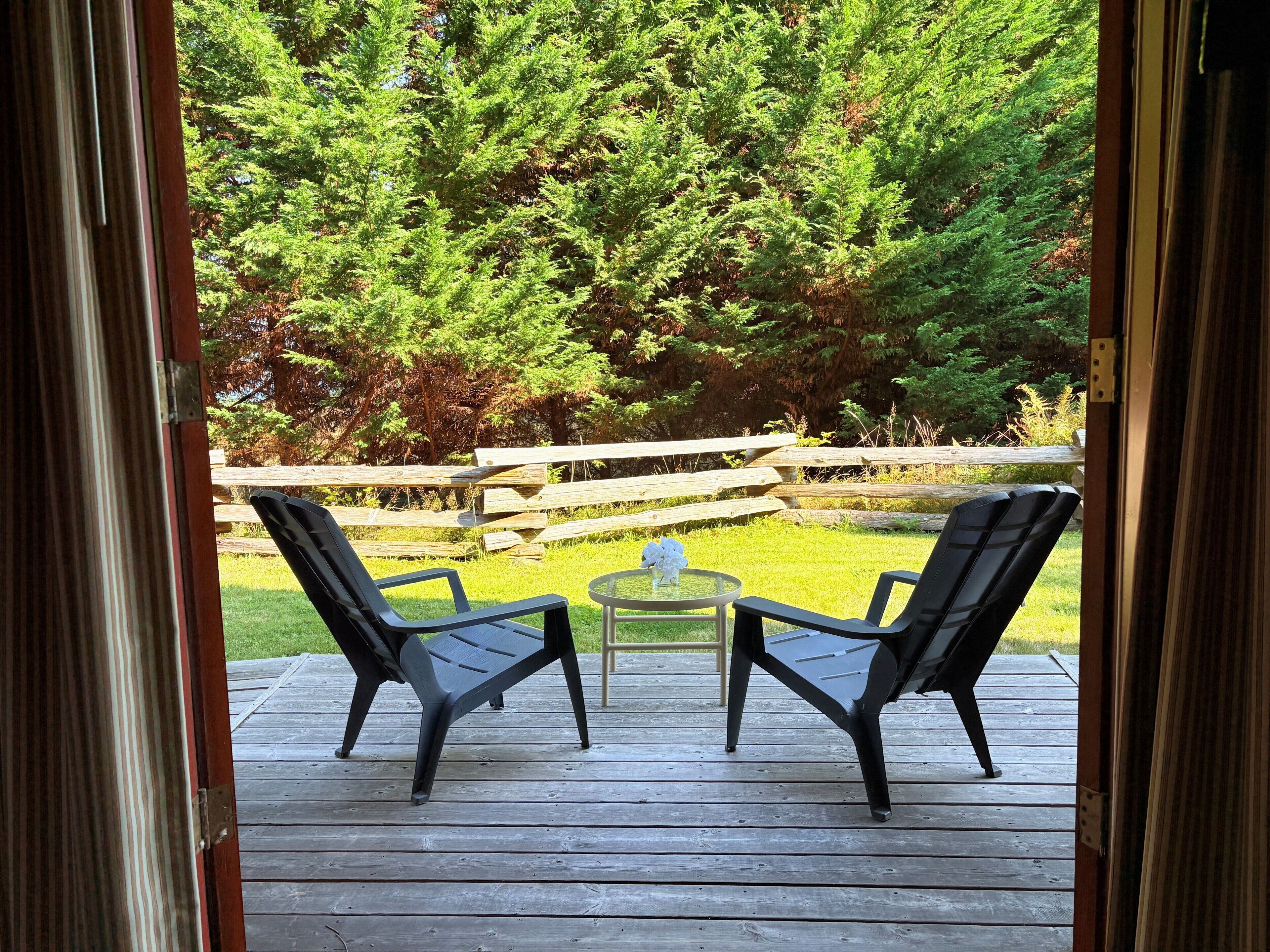 Une terrasse extérieure avec deux chaises et une petite table, donnant sur une clôture en bois et une forêt dense.