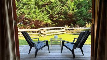 Une terrasse extérieure avec deux chaises et une petite table, donnant sur une clôture en bois et une forêt dense.