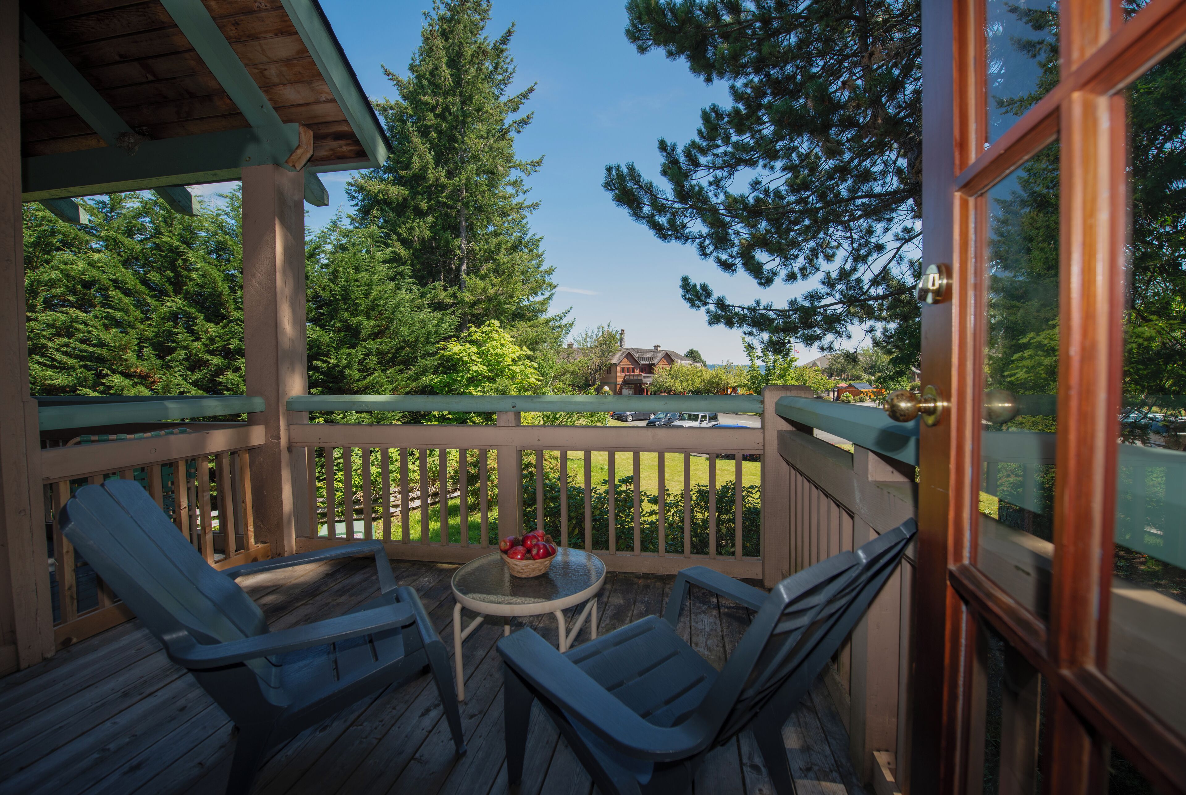 A wooden deck with two chairs and a small table, overlooking a grassy area and a distant building.