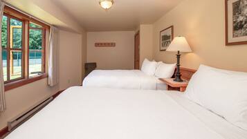 Habitación de hotel con dos camas, una mesita de noche con lámpara, una ventana con cortinas, un cuadro colgado en la pared y una puerta.