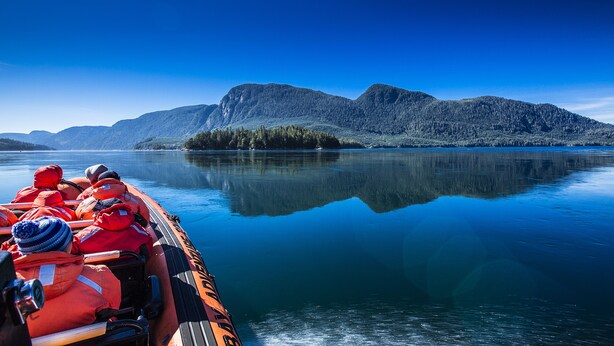 A boat with passengers wearing life jackets, a calm lake, and mountains in the background.