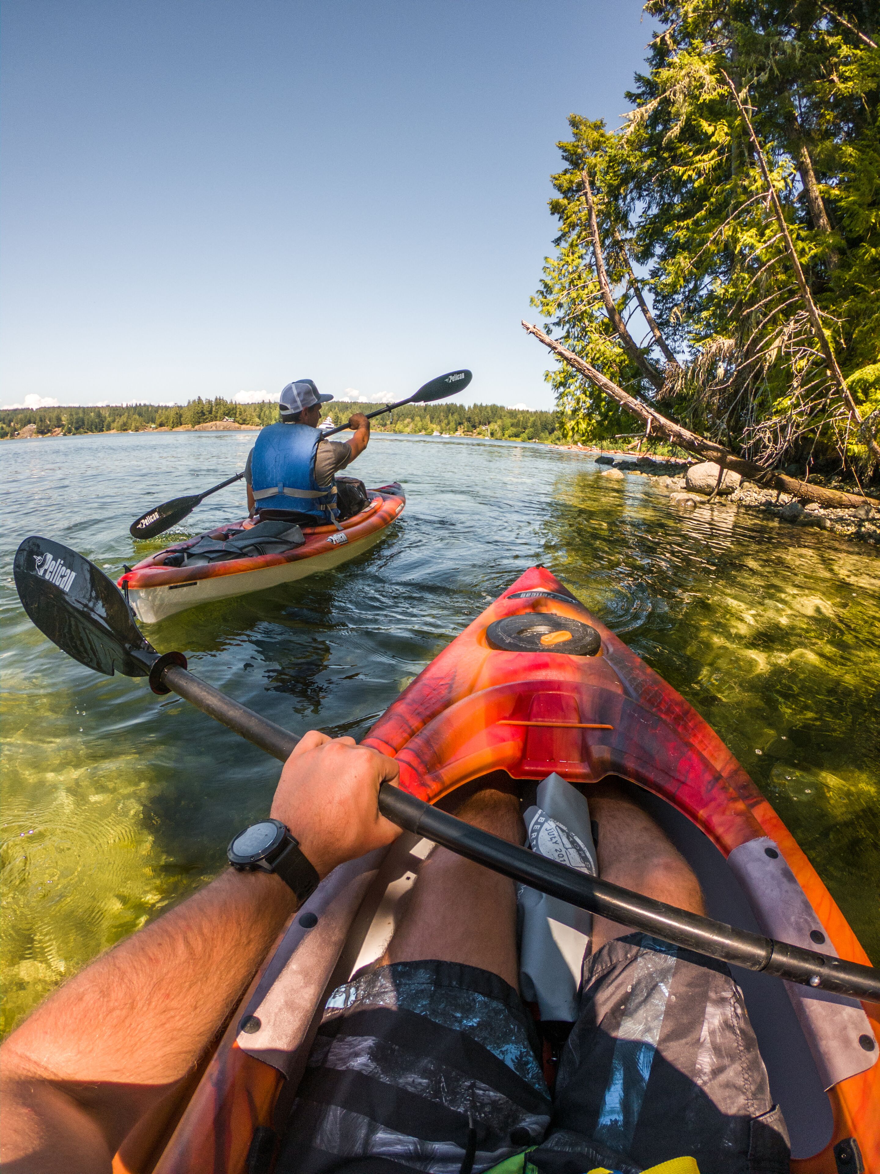 A kayak on a calm river with clear water and trees on the bank.
