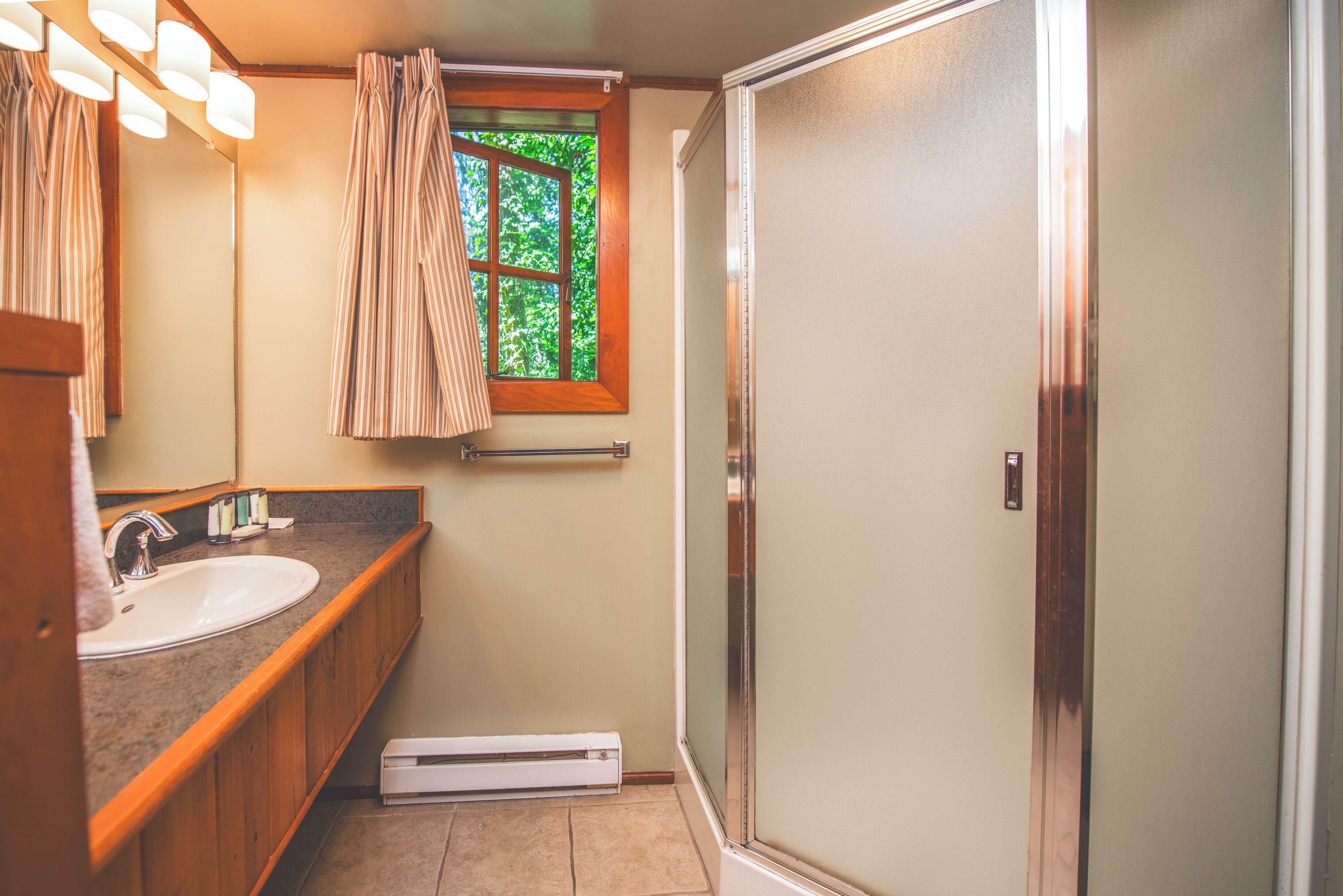 Un baño con lavamanos, espejo, toallero, ventana con cortinas y zona de ducha.
