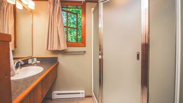Un baño con lavamanos, espejo, toallero, ventana con cortinas y zona de ducha.