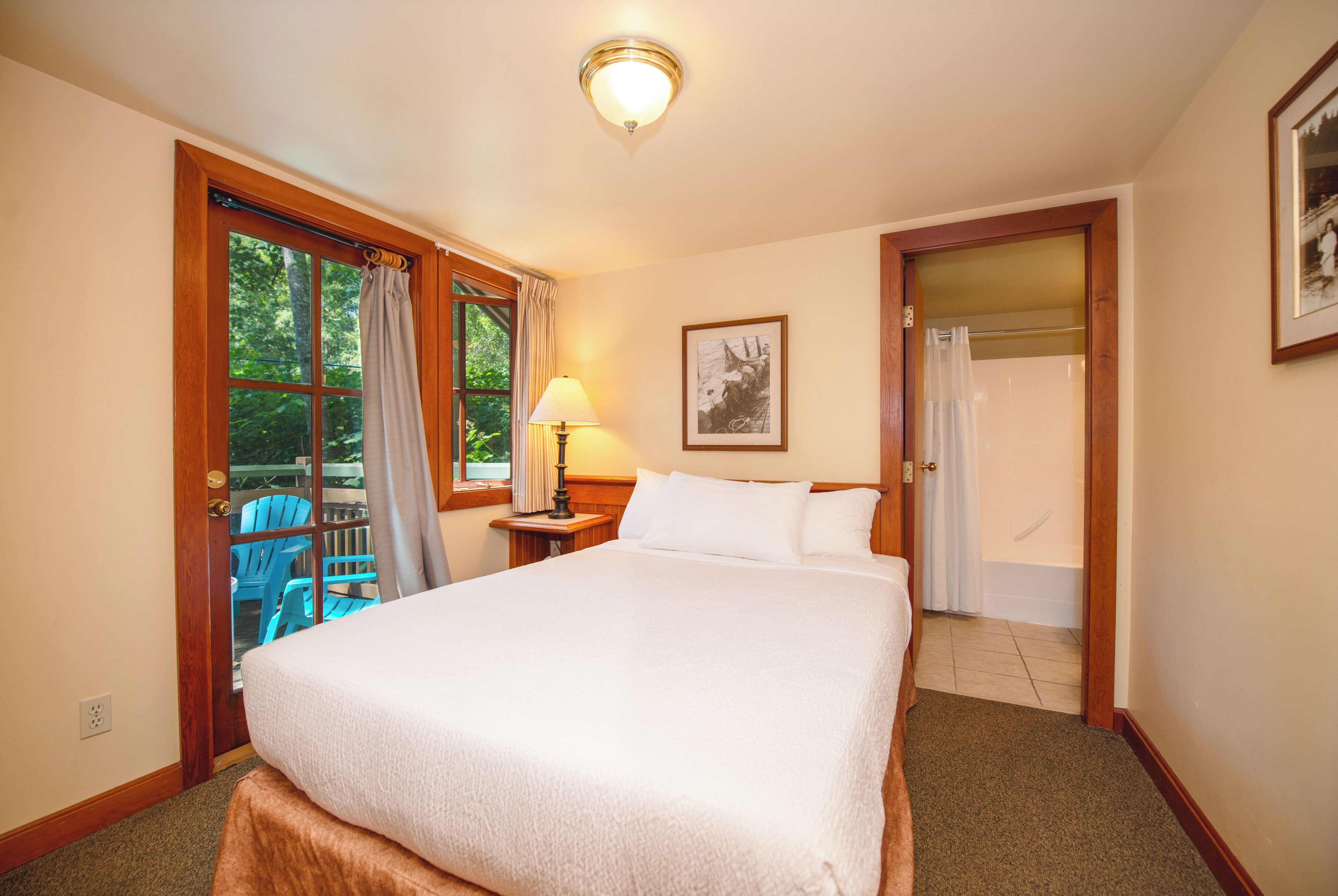 A hotel room with a large bed, a window with curtains, a lamp, and a framed picture on the wall.