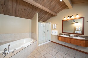 A bathroom with a large bathtub, a glass-enclosed shower, and wooden cabinets.